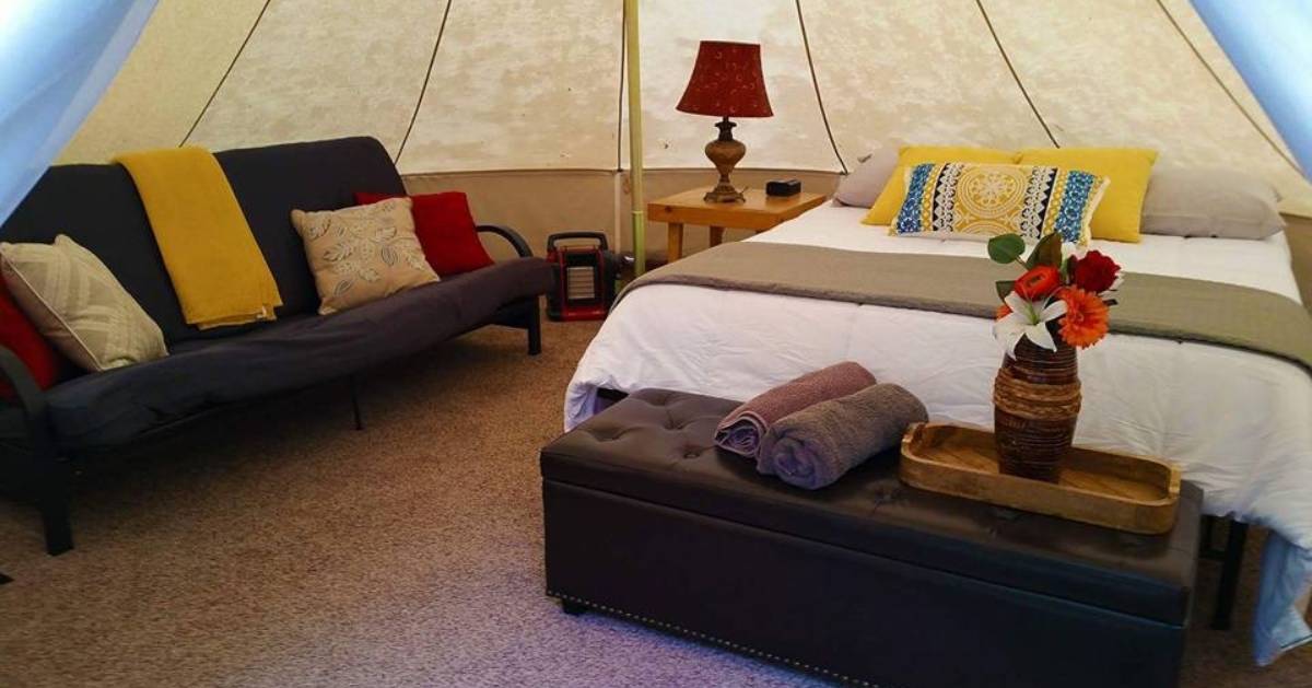 glamping tent with bed, sofa, pillows, and flowers
