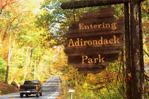 black truck driving by entering adirondack park sign among fall foliage