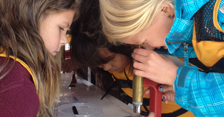 two girls, one looking through a microscope