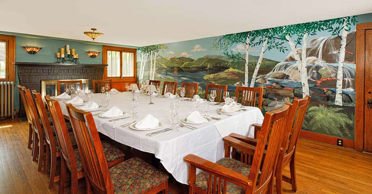 a room with a fireplace, a large table with dinnerware, and a wall sized mural of nature 