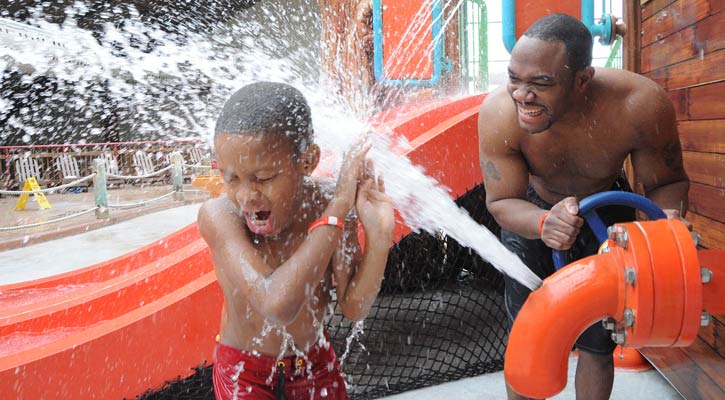 man splashing son with water coming out of a type of fire hydrant