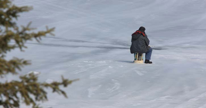 man sitting near ice fishing hole