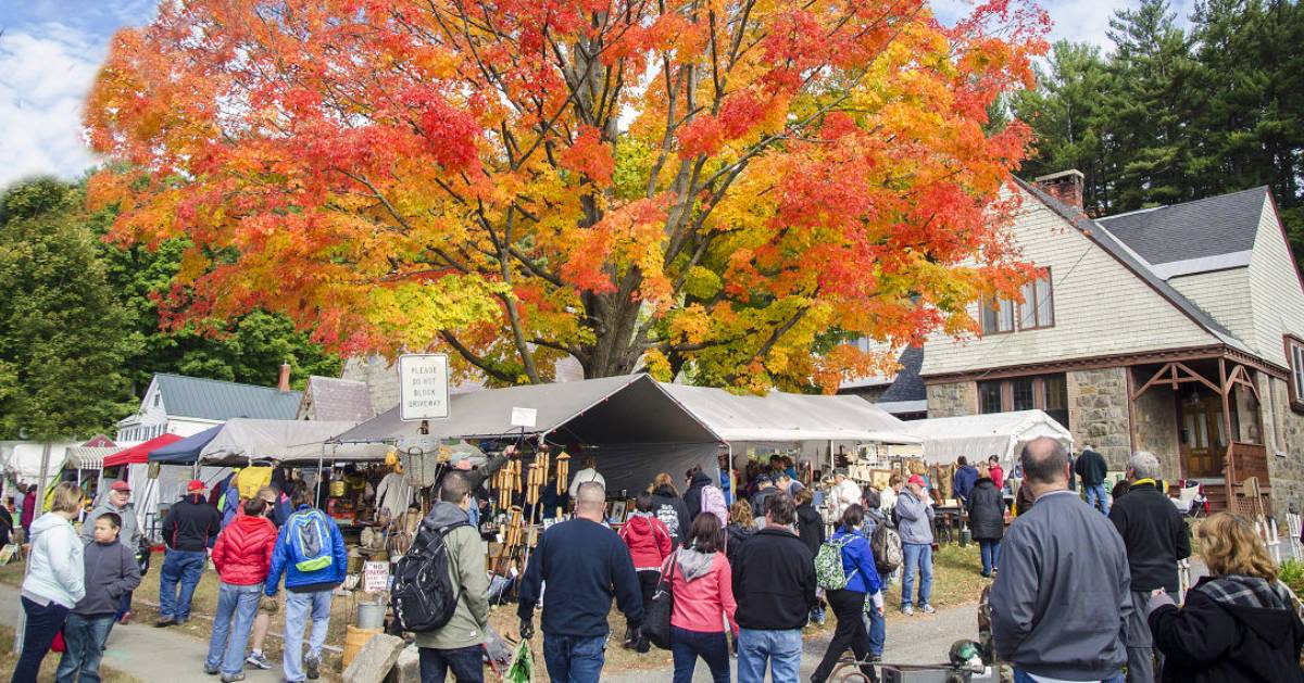 fall foliage on a tree and a garage sale happening nearby with a crowd of people