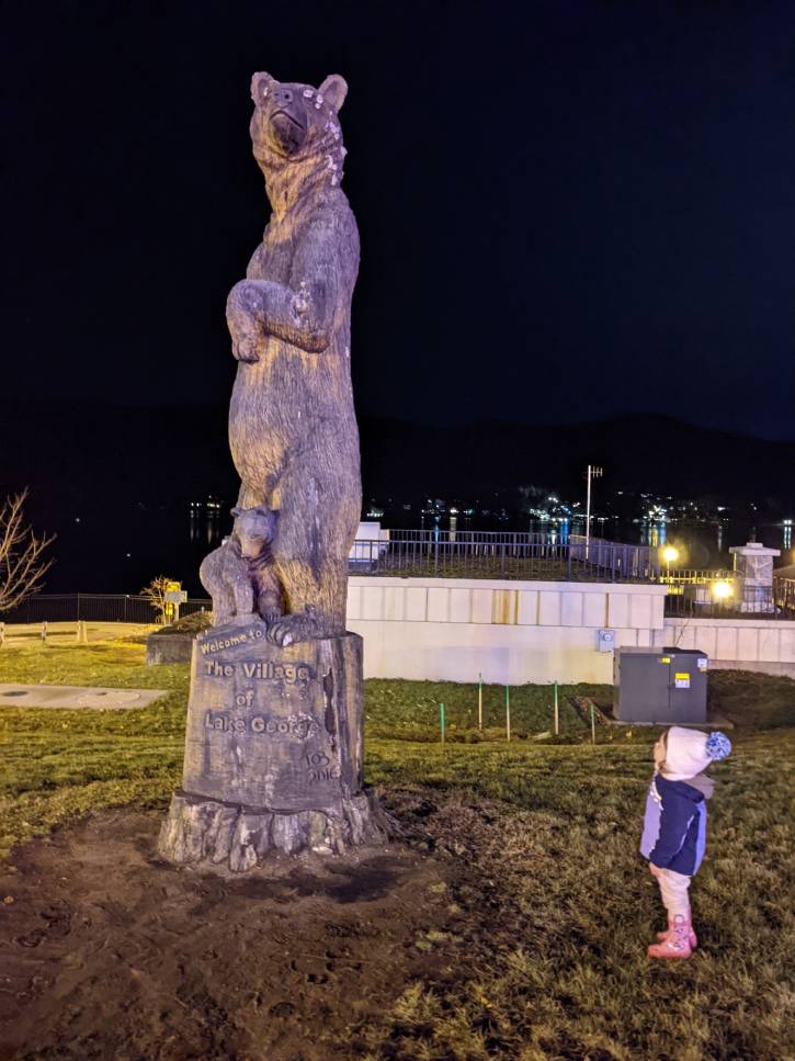 girl looks up at large bear statue at night