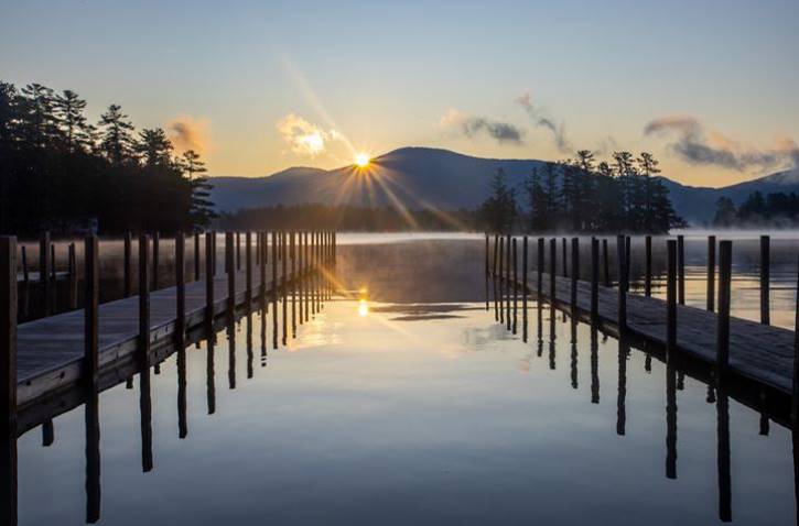 Sun rising behind mountains over lake with 2 docks