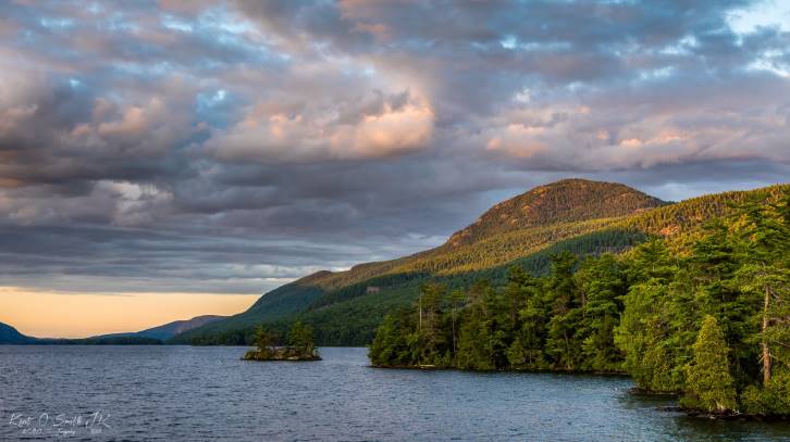 sun shining on mountain through clouds near lake