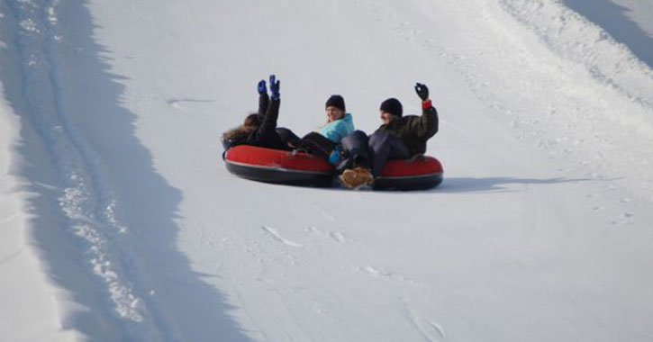 people riding down three snow tubes